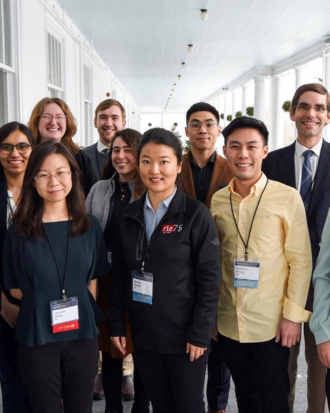 13 people in business attire pose for a group photo on a large, white covered porch