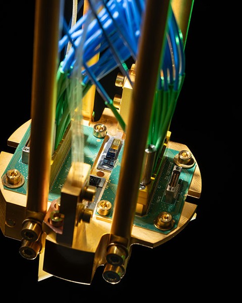 Close-up photo of a quantum repeater module mounted on a gold-plated copper assembly and connected to green printed circuit boards, with optical fibers routed up.