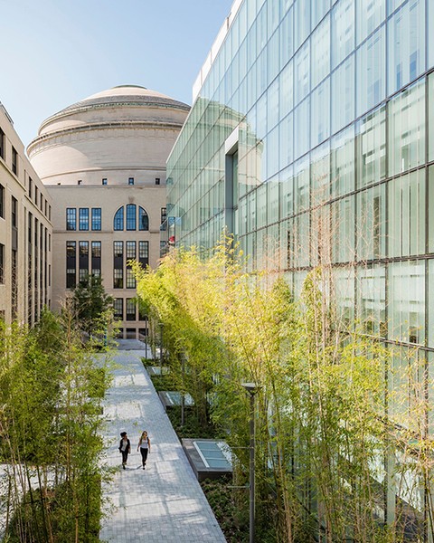 Exterior photo of the all-glass MIT.nano, at right; the brick Main Group building, at left; and a courtyard pathway down the middle, with MIT Dome in the background