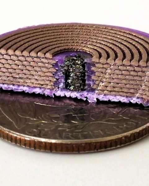 On top of a quarter sits a disc-like device chopped in half to show the interior: purple plastic is on outside, eight stacks of coiled copper-colored rods; and in the middle is a black substance.