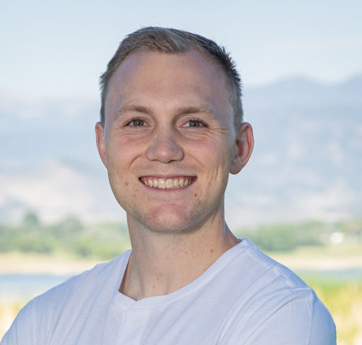 color photo of Samuel Karlson wearing a white shirt standing with mountains behind him in the distance