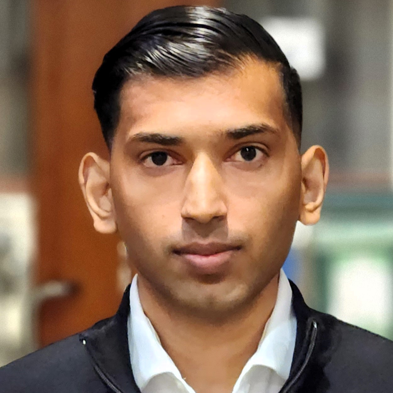 headshot portrait of Suraj Cheema a male with dark hair wearing white collar shirt and black zip up jacket
