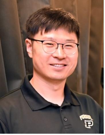 male with glasses wearing dark collared shirt in front of black fabric background