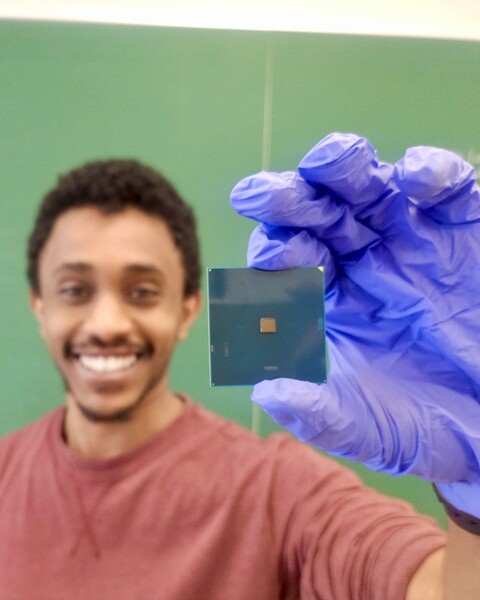 Natnael Kahssay, wearing nitrile gloves, smiles and holds up a computer chip for the camera.