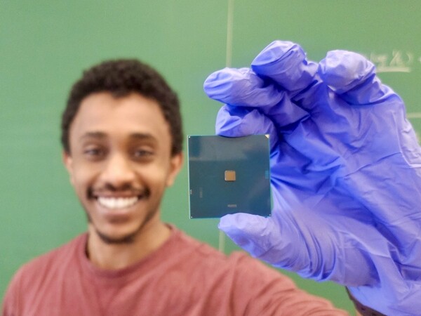 Natnael Kahssay, wearing nitrile gloves, smiles and holds up a computer chip for the camera.