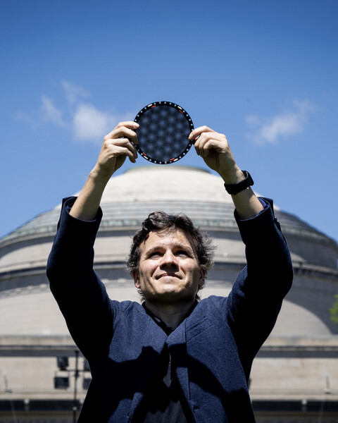 Pablo Jarillo-Herrero stands in front of the MIT dome, holding a circular wafer displaying moire patterns over his head