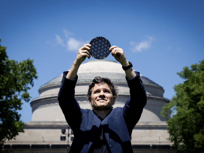 Pablo Jarillo-Herrero stands in front of the MIT dome, holding a circular wafer displaying moire patterns over his head