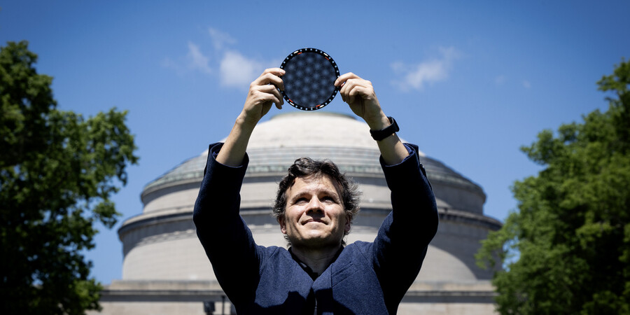 Pablo Jarillo-Herrero stands in front of the MIT dome, holding a circular wafer displaying moire patterns over his head